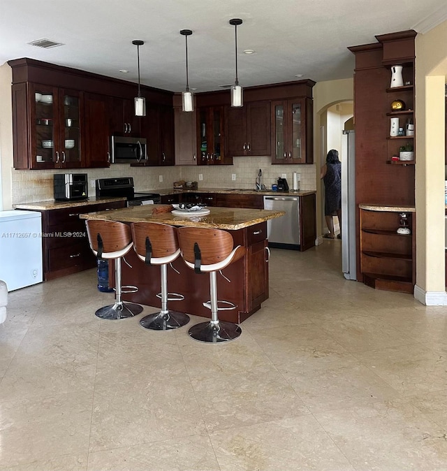 kitchen featuring pendant lighting, a center island, dark stone counters, dark brown cabinets, and stainless steel appliances