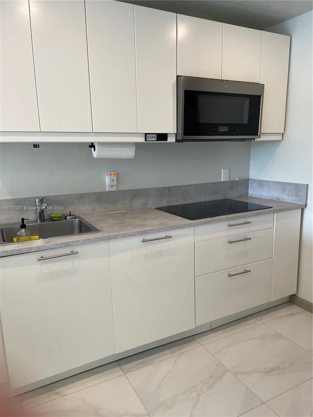 kitchen with black electric stovetop, white cabinetry, and sink