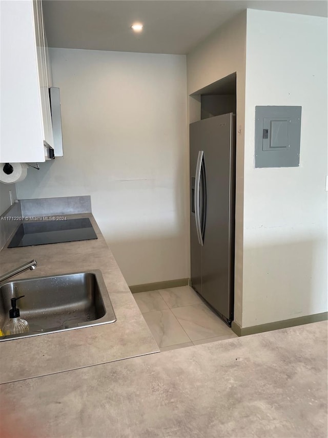 kitchen featuring electric panel, sink, stainless steel fridge, black electric cooktop, and white cabinetry