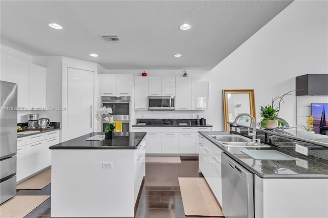 kitchen with appliances with stainless steel finishes, a textured ceiling, sink, a center island, and white cabinetry