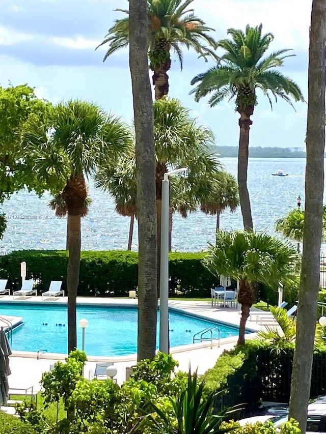 pool featuring a patio area, a water view, and fence