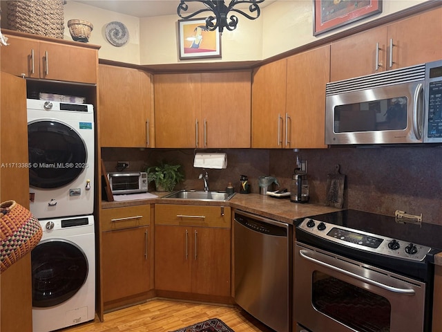 kitchen with light wood finished floors, decorative backsplash, appliances with stainless steel finishes, stacked washer / dryer, and a sink