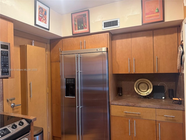 kitchen with stainless steel appliances, brown cabinetry, dark countertops, and visible vents