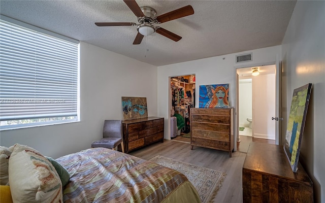 bedroom with a walk in closet, ceiling fan, light wood-type flooring, a textured ceiling, and a closet