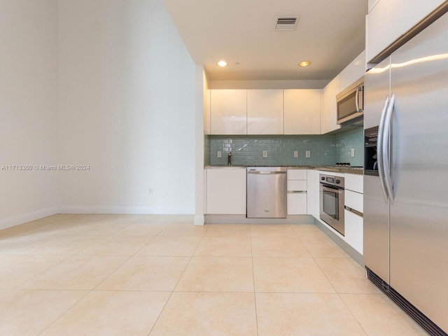 kitchen featuring tasteful backsplash, stainless steel appliances, sink, light tile patterned floors, and white cabinetry