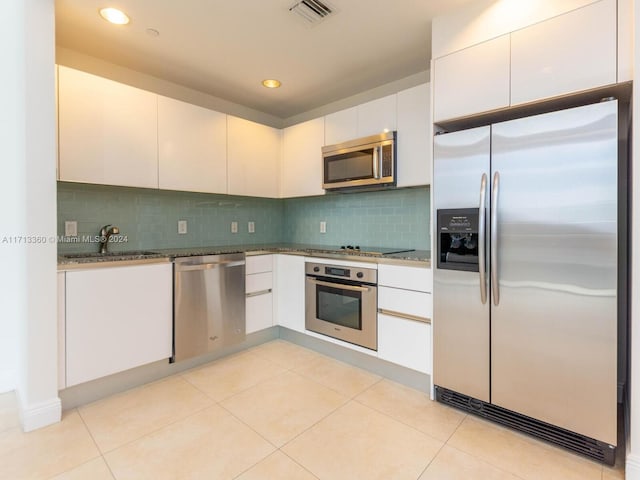 kitchen featuring appliances with stainless steel finishes, sink, dark stone countertops, white cabinetry, and light tile patterned flooring