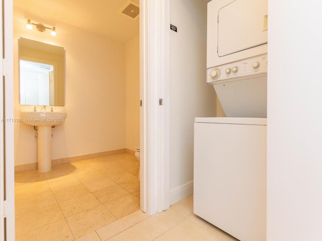 clothes washing area featuring light tile patterned floors and stacked washer and clothes dryer