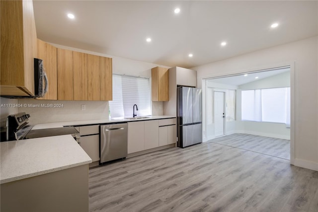 kitchen featuring light stone countertops, sink, stainless steel appliances, white cabinets, and light wood-type flooring