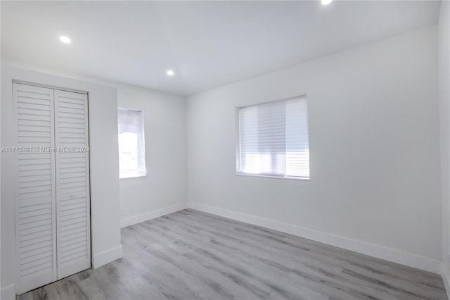 unfurnished bedroom with multiple windows, a closet, and light hardwood / wood-style floors