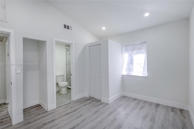 unfurnished bedroom featuring vaulted ceiling, light hardwood / wood-style flooring, a closet, and ensuite bath