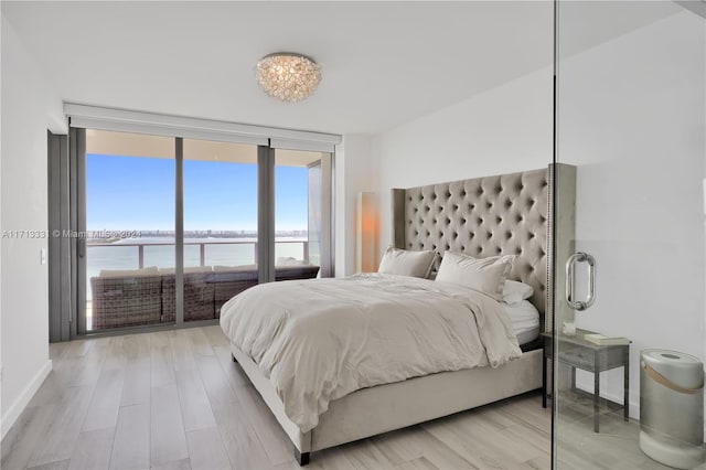 bedroom with expansive windows, a water view, and light hardwood / wood-style flooring