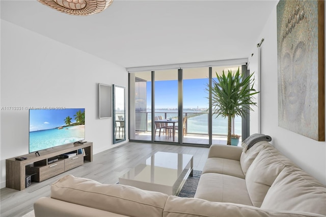 living room featuring a water view, light wood-type flooring, and a wall of windows