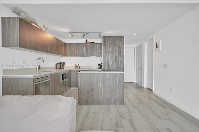 kitchen with light wood-type flooring, rail lighting, stainless steel dishwasher, sink, and a kitchen island