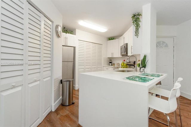 kitchen featuring appliances with stainless steel finishes, light wood-type flooring, a breakfast bar, sink, and white cabinetry