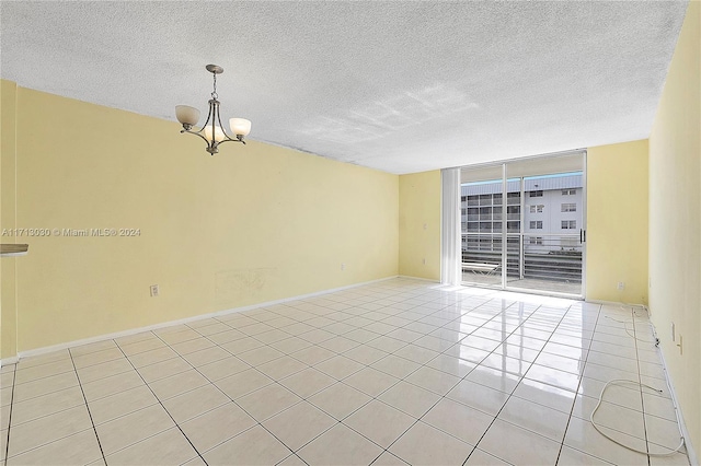 tiled empty room with a notable chandelier, a wall of windows, and a textured ceiling