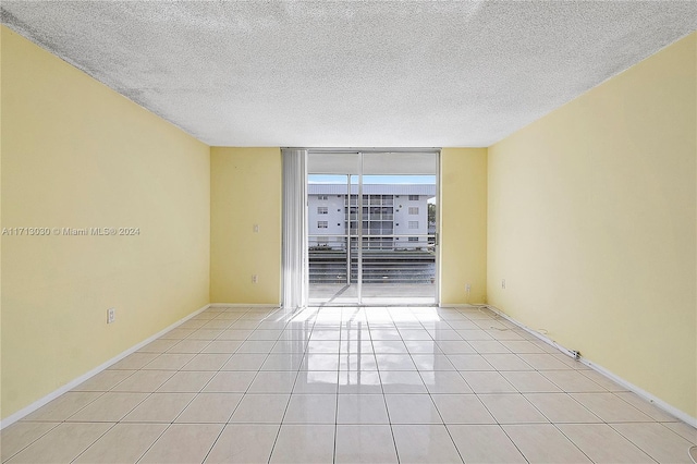 tiled empty room featuring floor to ceiling windows and a textured ceiling