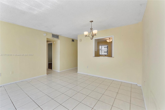 unfurnished room featuring a textured ceiling, an inviting chandelier, and light tile patterned flooring