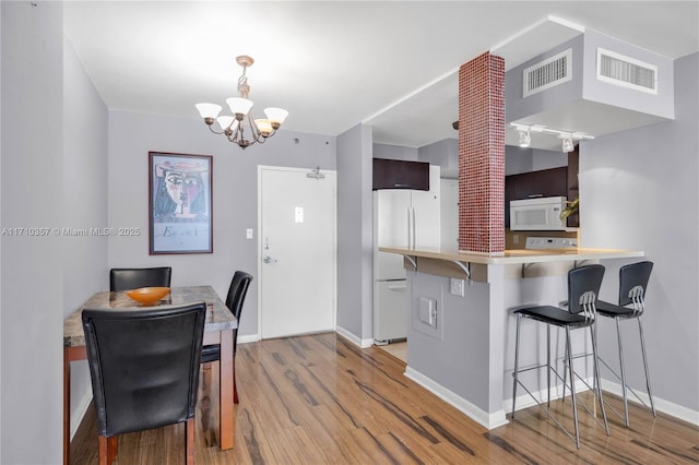 kitchen with a breakfast bar, white appliances, a notable chandelier, light hardwood / wood-style floors, and kitchen peninsula