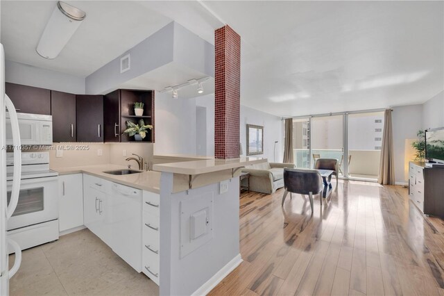 kitchen with dark brown cabinetry, sink, kitchen peninsula, white appliances, and white cabinets