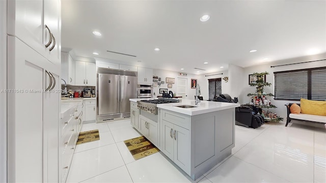 kitchen featuring white cabinetry, tasteful backsplash, a kitchen island with sink, light tile patterned floors, and appliances with stainless steel finishes