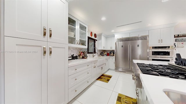 kitchen featuring backsplash, sink, light tile patterned flooring, white cabinetry, and stainless steel appliances