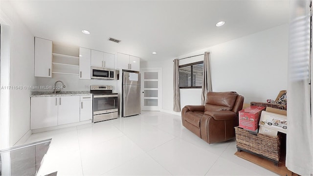 kitchen featuring sink, light stone countertops, appliances with stainless steel finishes, light tile patterned flooring, and white cabinetry