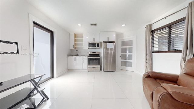 kitchen with sink, light tile patterned floors, appliances with stainless steel finishes, light stone counters, and white cabinetry