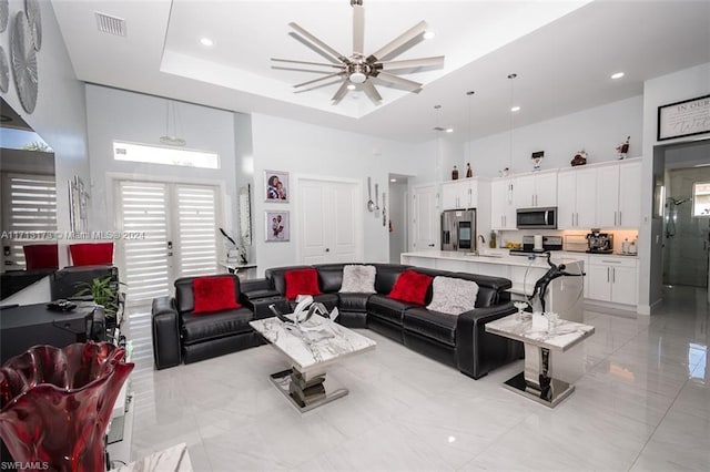 living room with a tray ceiling, ceiling fan, sink, and a high ceiling