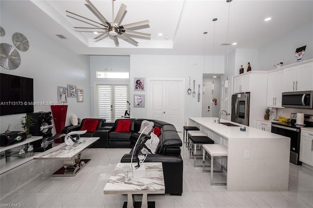 living room with ceiling fan, sink, and a tray ceiling