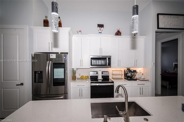 kitchen featuring appliances with stainless steel finishes, light stone counters, sink, decorative light fixtures, and white cabinetry