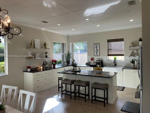 kitchen with sink, a kitchen island, light tile patterned flooring, a breakfast bar area, and white cabinets