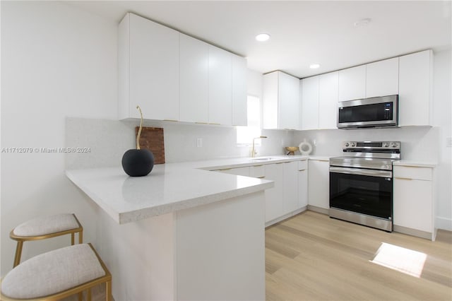 kitchen with kitchen peninsula, a kitchen breakfast bar, stainless steel appliances, sink, and white cabinetry