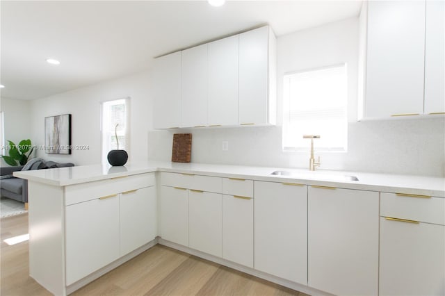 kitchen featuring white cabinetry, sink, tasteful backsplash, light hardwood / wood-style flooring, and kitchen peninsula