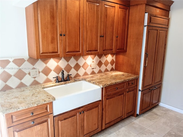 kitchen featuring light stone counters, sink, tasteful backsplash, and paneled built in refrigerator