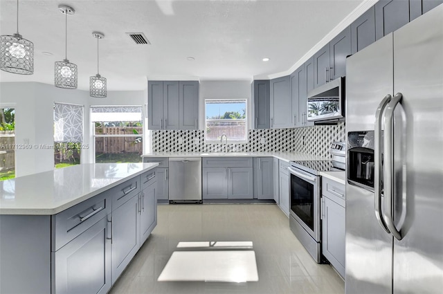 kitchen with gray cabinets, appliances with stainless steel finishes, pendant lighting, sink, and plenty of natural light