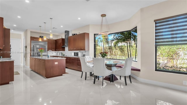 kitchen with pendant lighting, sink, wall chimney exhaust hood, light stone countertops, and an island with sink