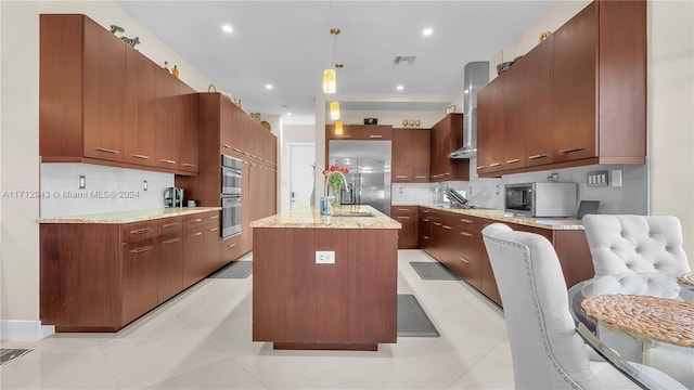 kitchen featuring a kitchen island with sink, wall chimney range hood, sink, appliances with stainless steel finishes, and decorative light fixtures