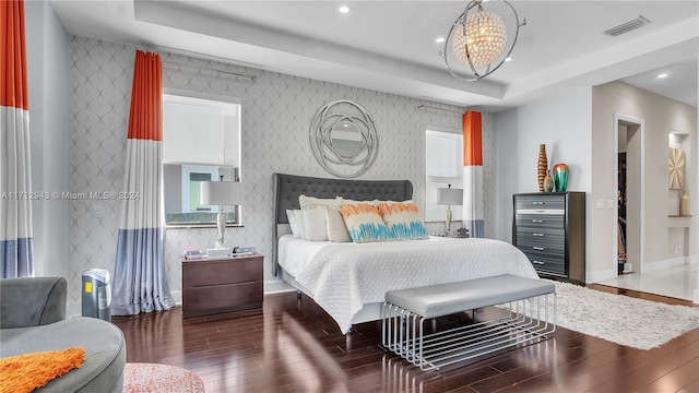 bedroom featuring dark hardwood / wood-style flooring, a tray ceiling, and a notable chandelier