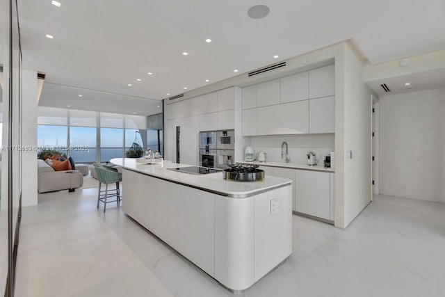 kitchen featuring floor to ceiling windows, sink, an island with sink, black electric cooktop, and white cabinets