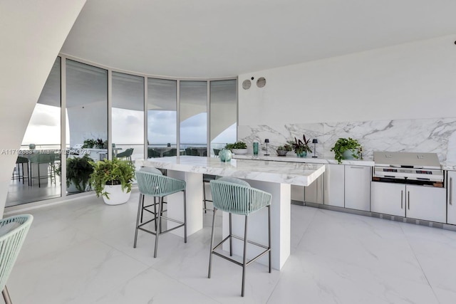 kitchen featuring a center island, light stone countertops, white cabinetry, a wall of windows, and a breakfast bar area