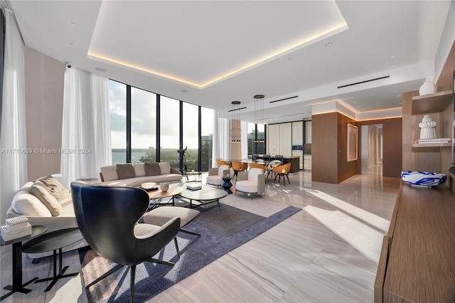 living room with expansive windows, a raised ceiling, and a water view