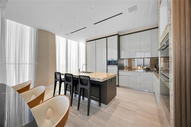 kitchen featuring sink, a center island with sink, a wall of windows, white cabinets, and a breakfast bar area