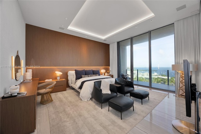 bedroom featuring access to outside, floor to ceiling windows, wood walls, and a raised ceiling