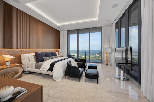 bedroom with access to outside, a raised ceiling, floor to ceiling windows, and wooden walls