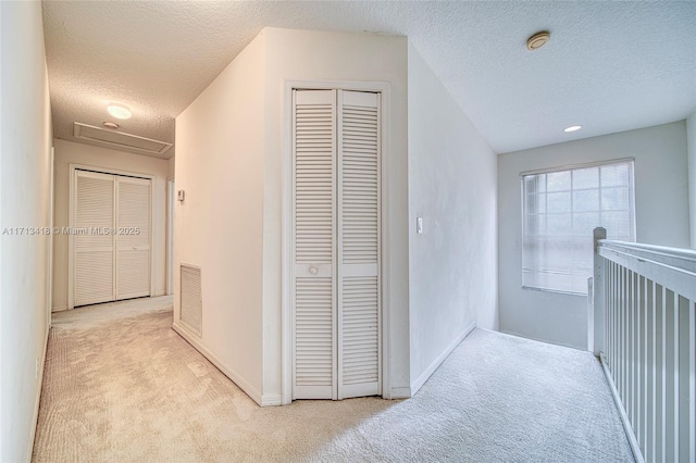 corridor featuring light colored carpet and a textured ceiling