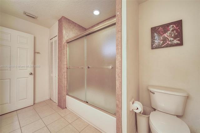 bathroom featuring shower / bath combination with glass door, a textured ceiling, tile patterned flooring, and toilet