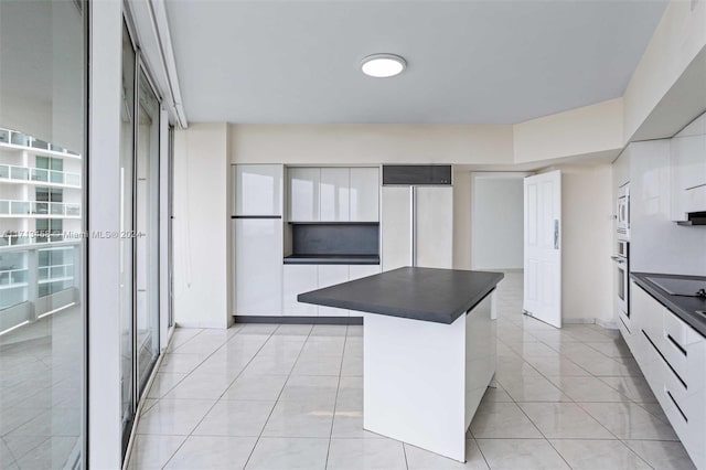 kitchen with paneled refrigerator, light tile patterned floors, white cabinets, a center island, and oven