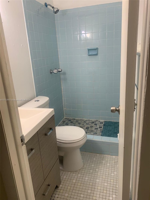 bathroom with tile patterned flooring, vanity, toilet, and a tile shower