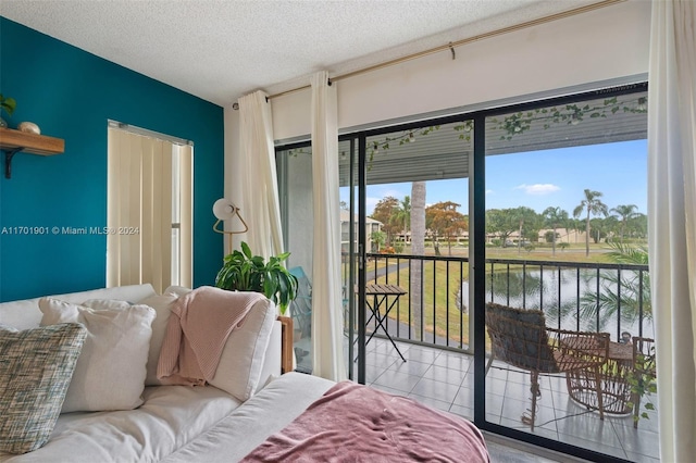 bedroom featuring access to exterior, light tile patterned floors, a water view, and a textured ceiling