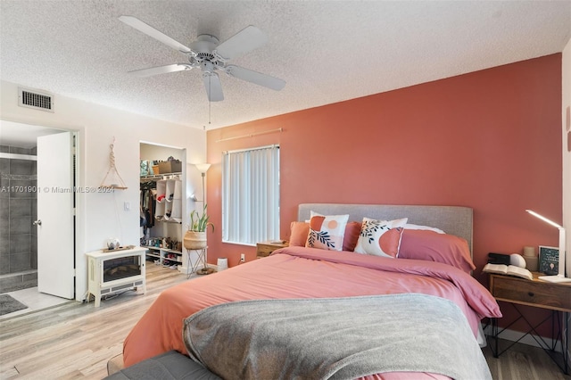 bedroom with ensuite bath, ceiling fan, light wood-type flooring, a textured ceiling, and a closet